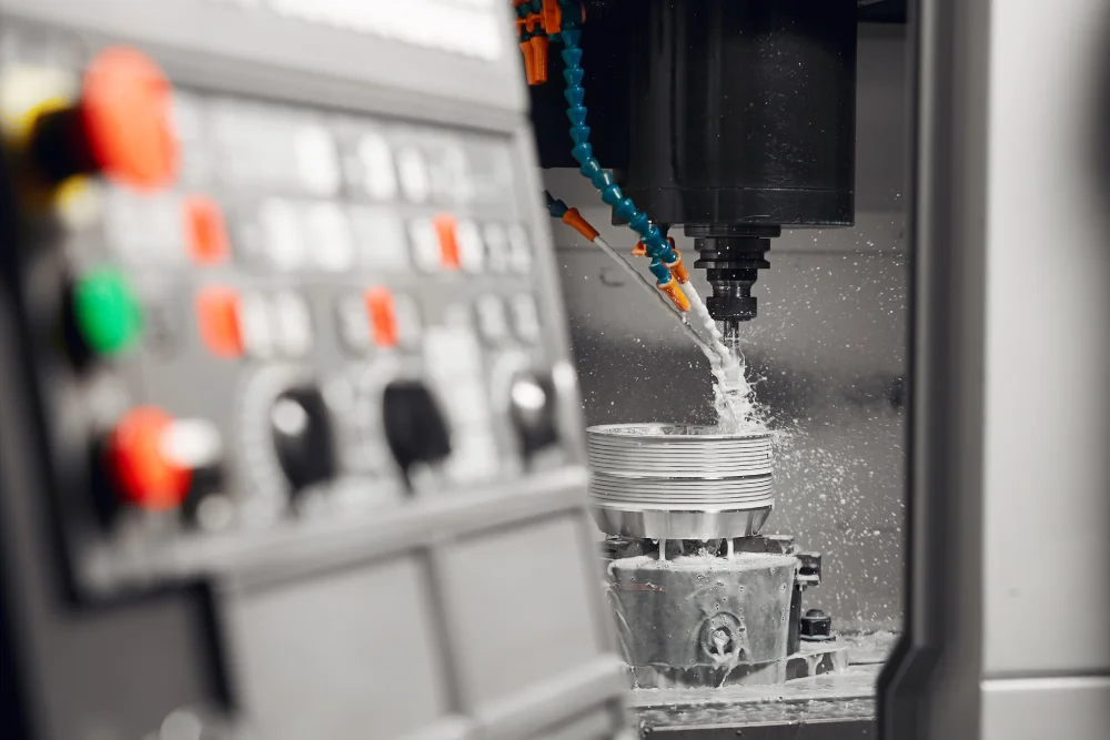 Eine CNC-Maschine bei Maletz & Esser in Düren schneidet ein Metallteil für die zertifizierte Fertigung, während Kühlflüssigkeit auf das Werkstück gesprüht wird. Im Vordergrund ist das Bedienfeld zu sehen, das leicht unscharf ist.